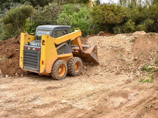 A yellow skid steer is moving dirt in a dirt field.