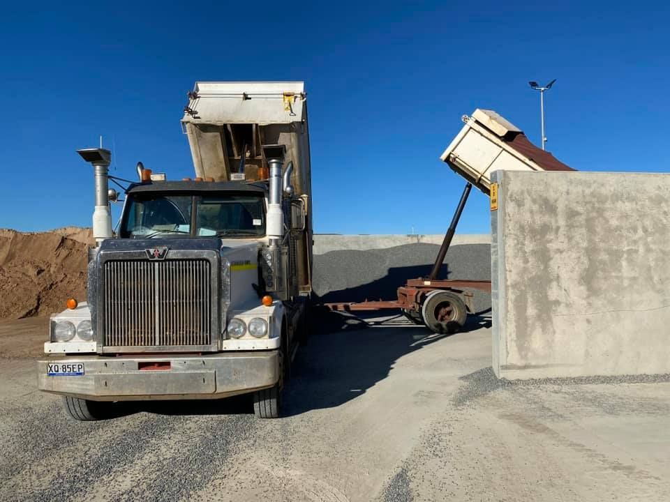 A dump truck is being loaded with gravel in a gravel yard