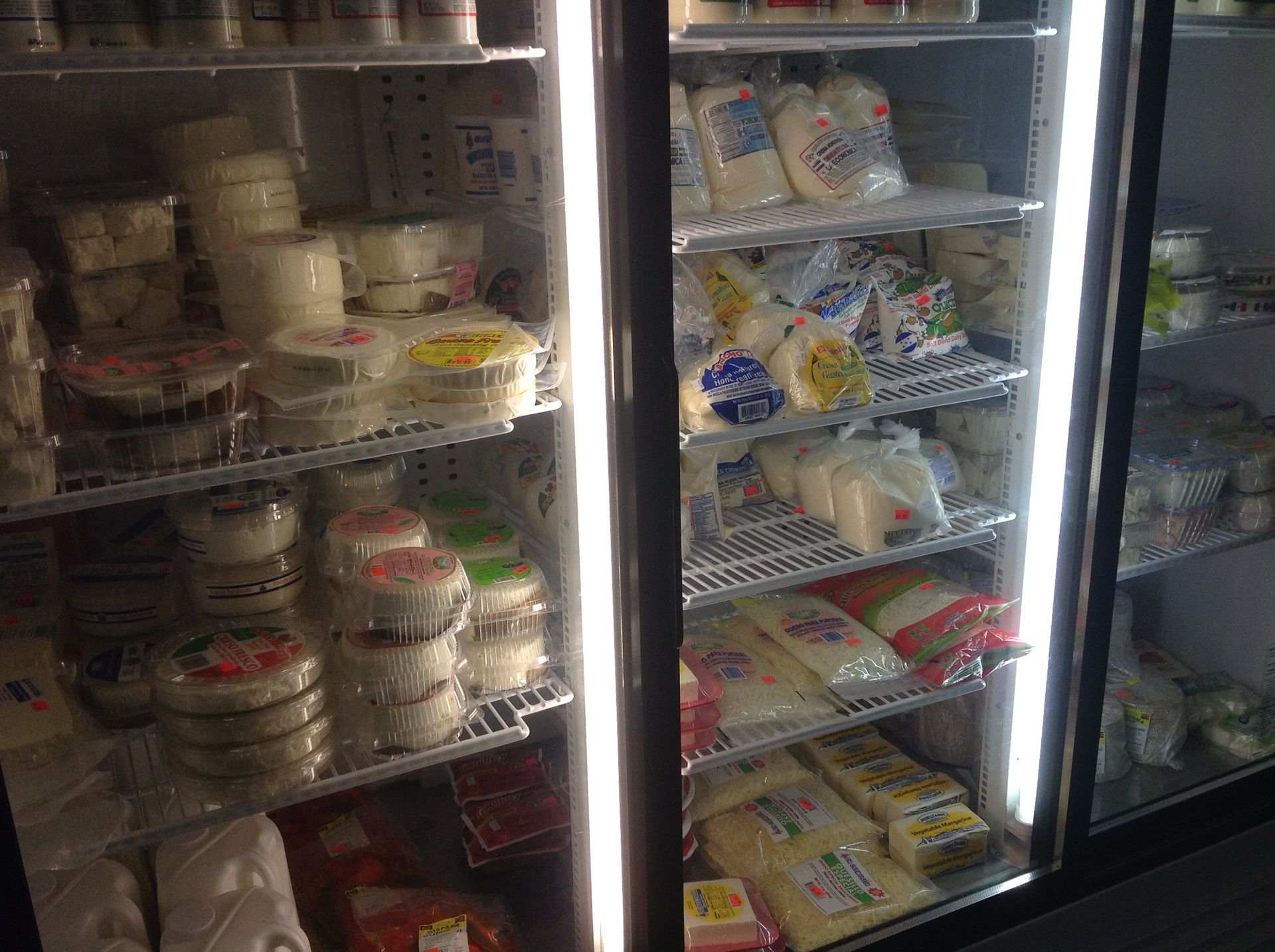 Glass refrigerator filled with various cheeses on shelves.