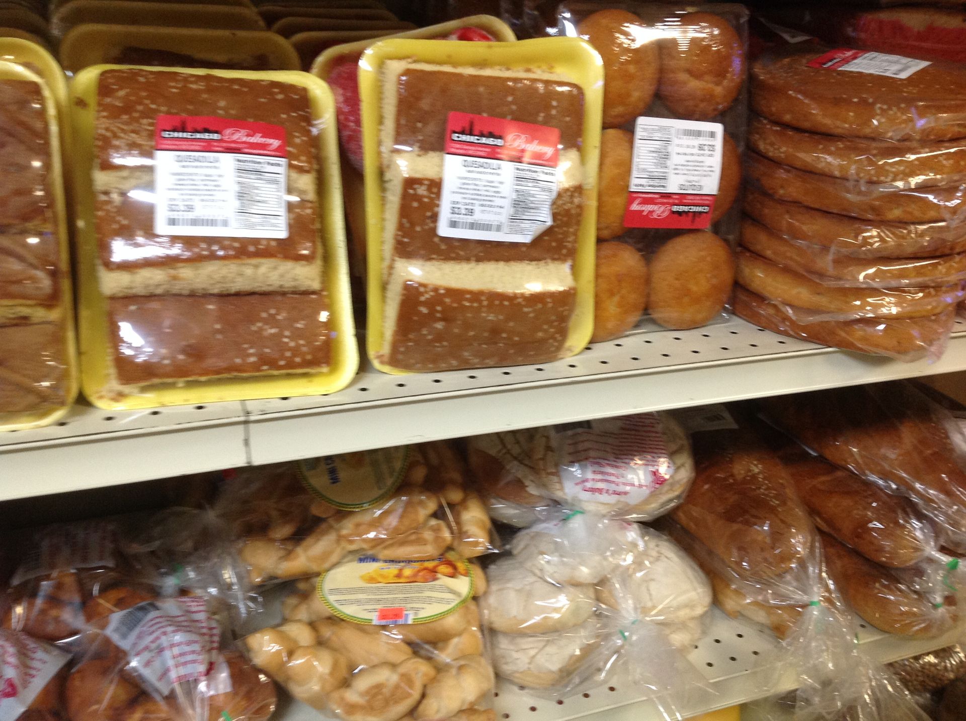 Packaged baked goods on a store shelf, including bread, buns, and cookies, labeled with price tags.