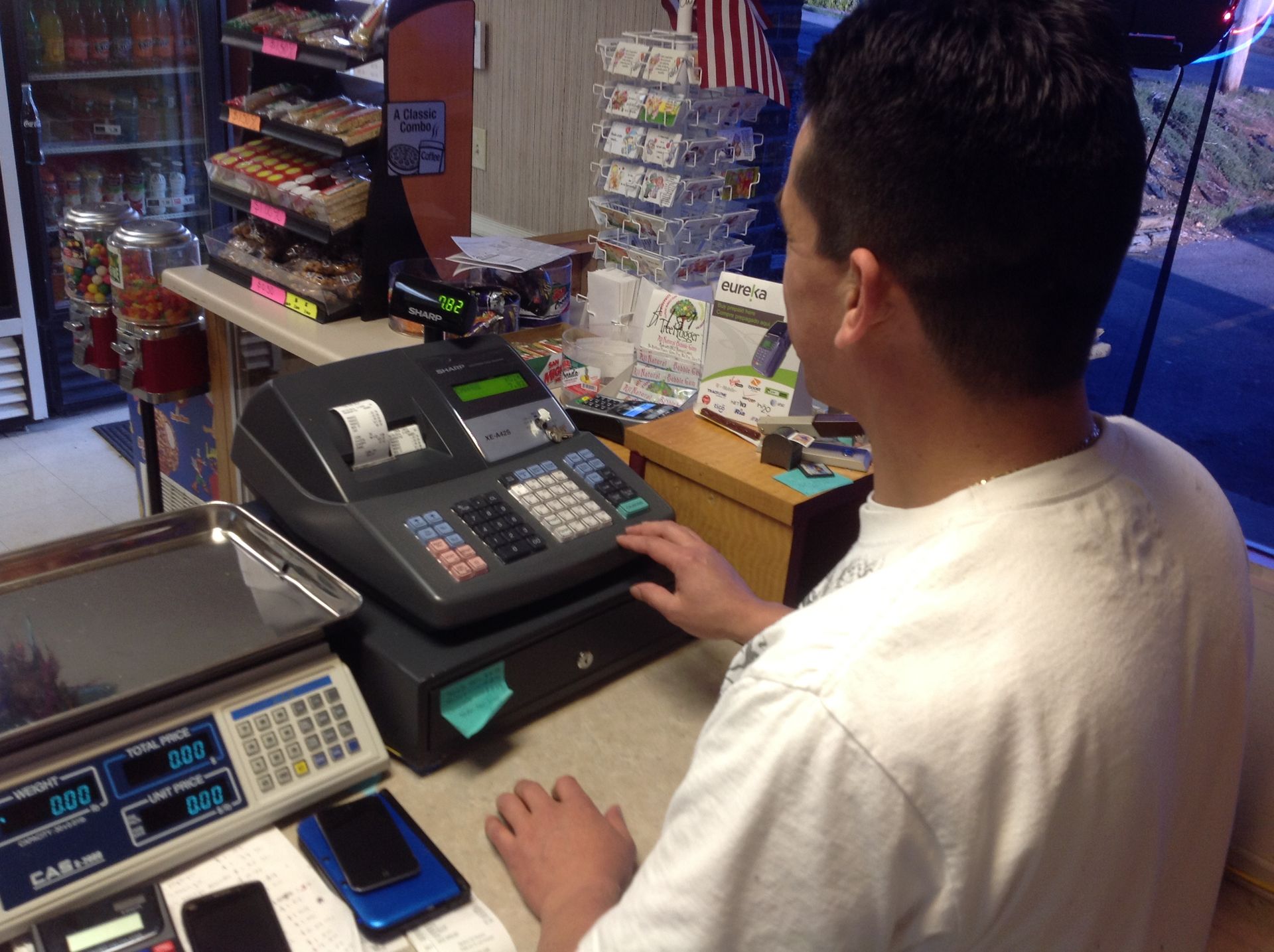 Person at a cash register in a store. They are entering information while looking forward. Scale and products visible.