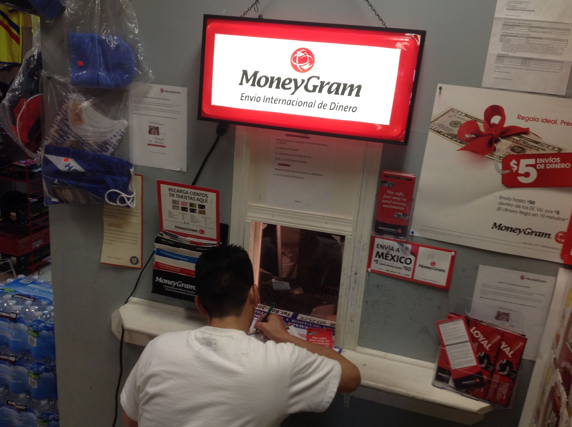Person at MoneyGram counter, writing. Signage includes MoneyGram logo and promotional materials.