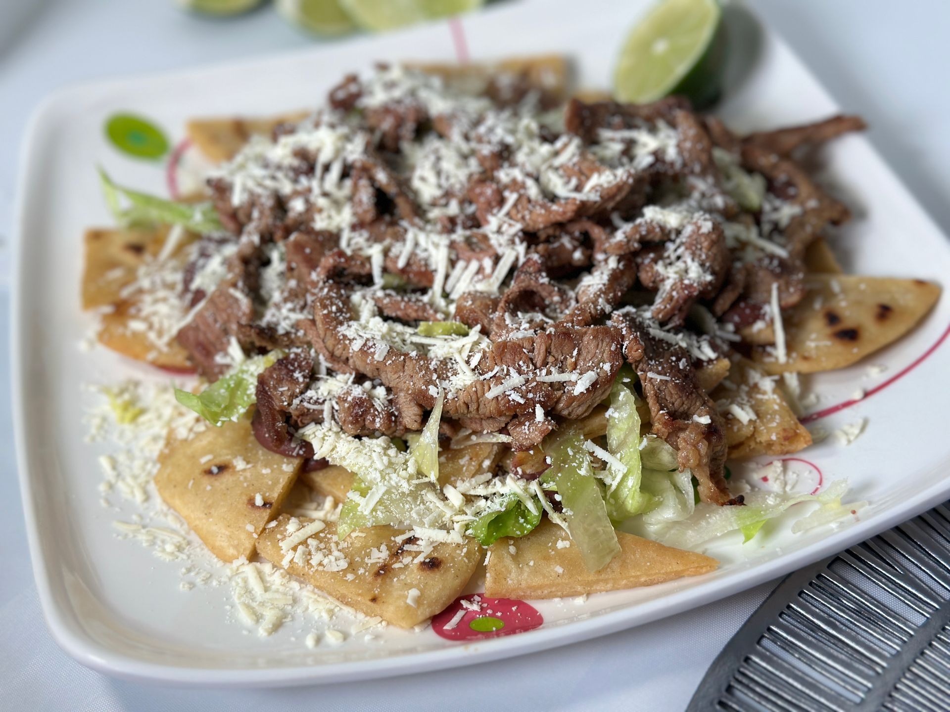 Steak chilaquiles with shredded lettuce and cheese on a white plate, lime wedges.