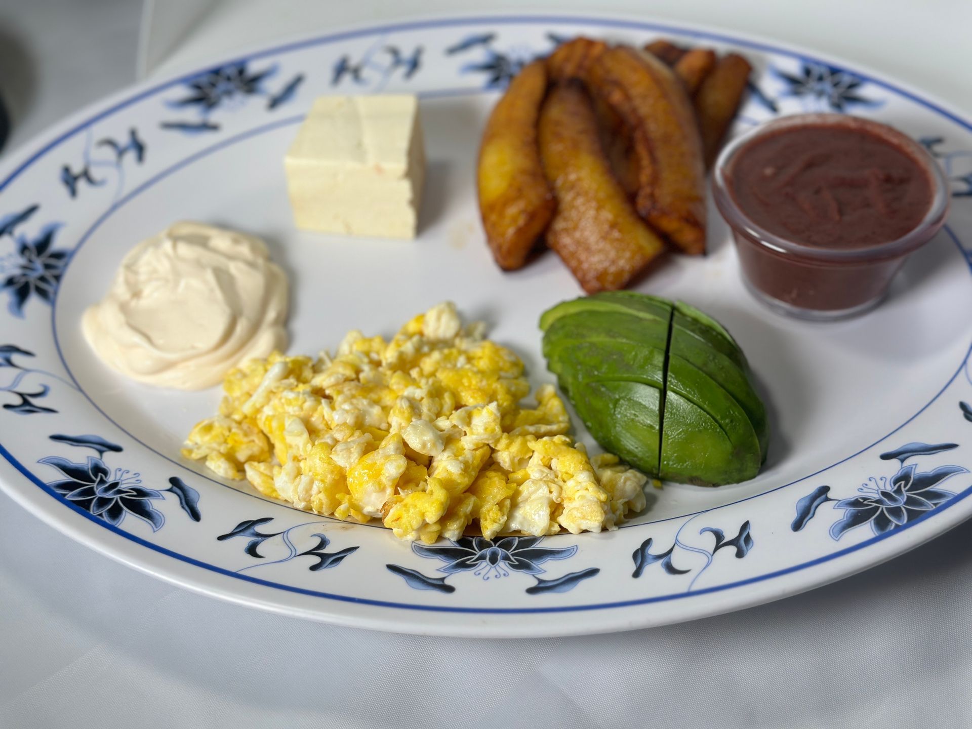 Plate of scrambled eggs, avocado, fried plantains, cheese, beans, and sour cream.