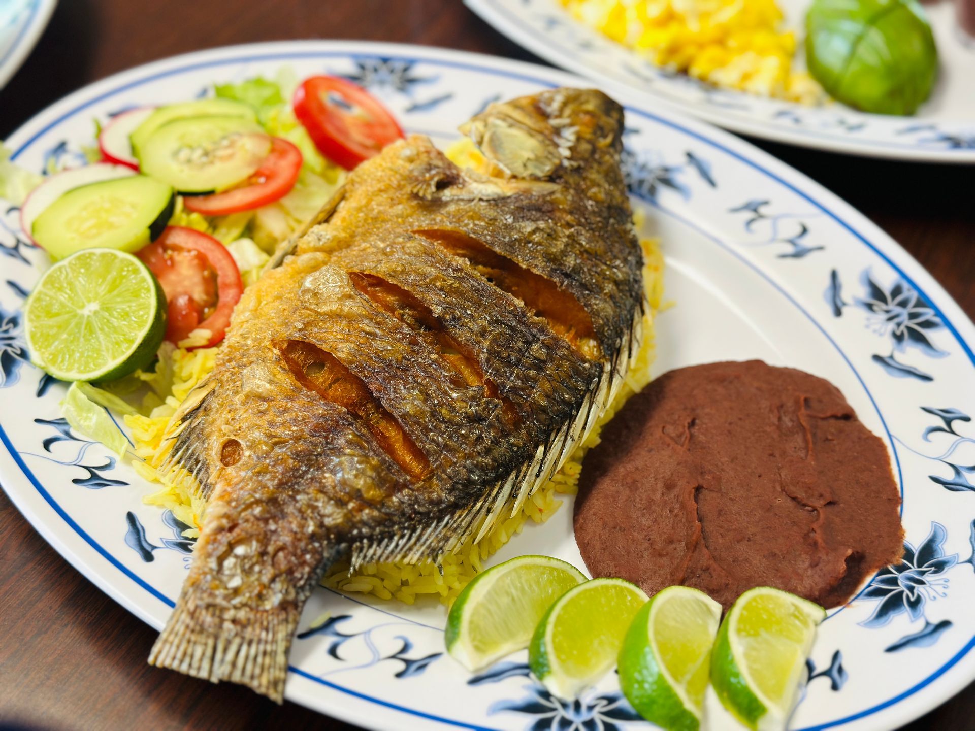 Fried whole fish on a plate with rice, refried beans, and lime slices. Salad on the side.