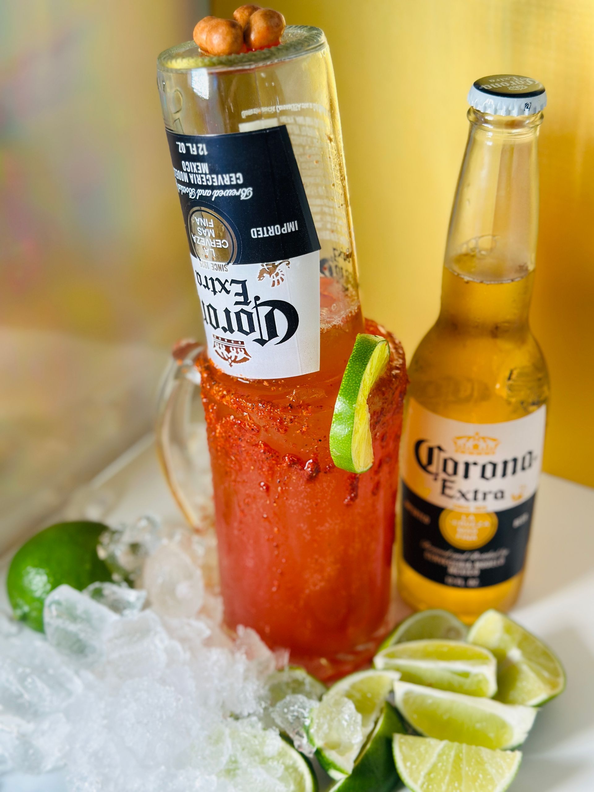 Corona beer cocktail with bottle in a red-rimmed glass, lime, and ice.
