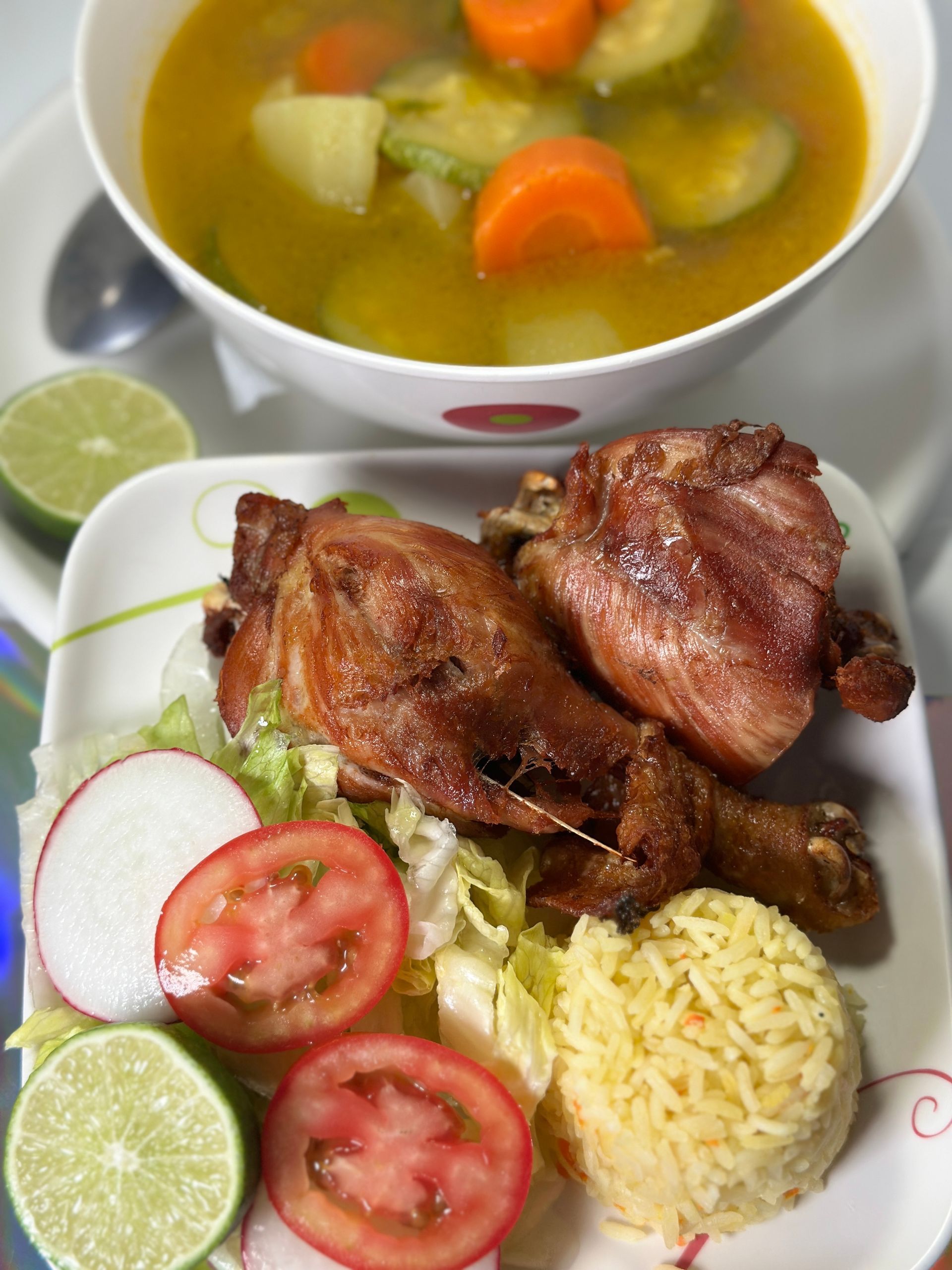 Plate with fried chicken, rice, salad, and lime, served with soup.