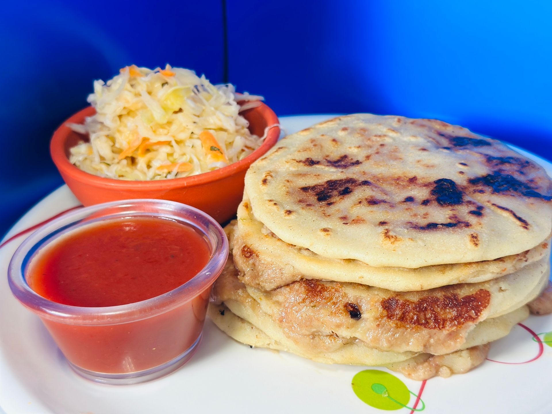 Stack of pupusas with curtido and tomato sauce in small bowls.