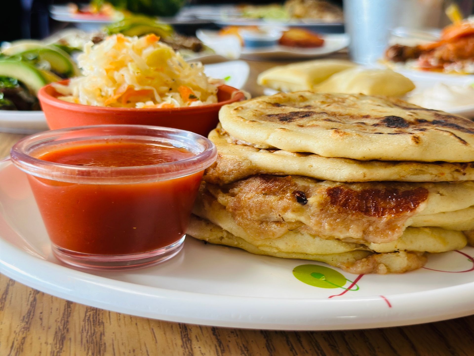 Stack of pupusas with red sauce and slaw, served on a white plate.