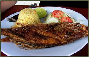 Fried whole fish with yellow rice, lime wedge, and salad on a white plate.