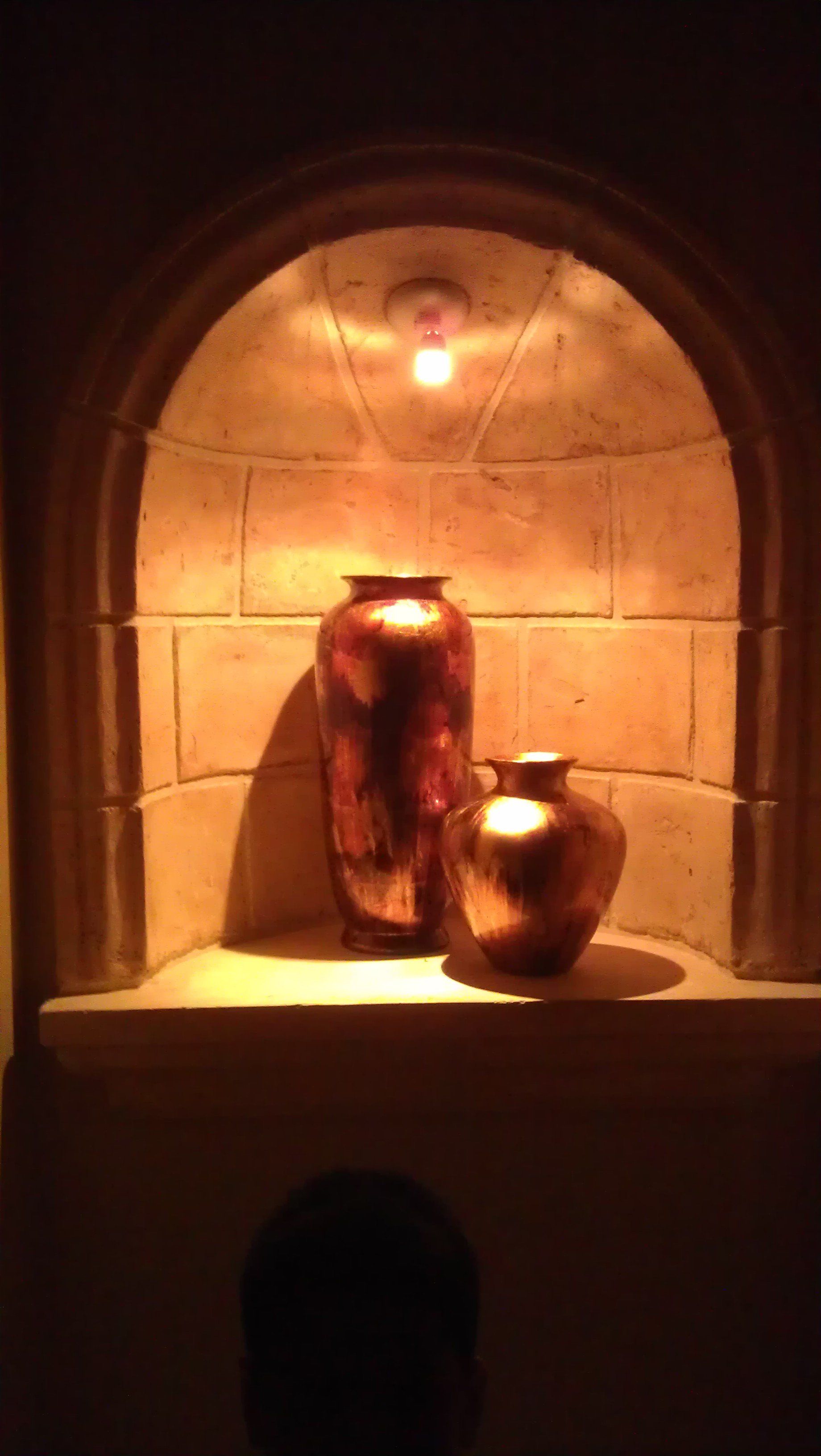Ambient accent light shining on two pieces of pottery in a stone nook.