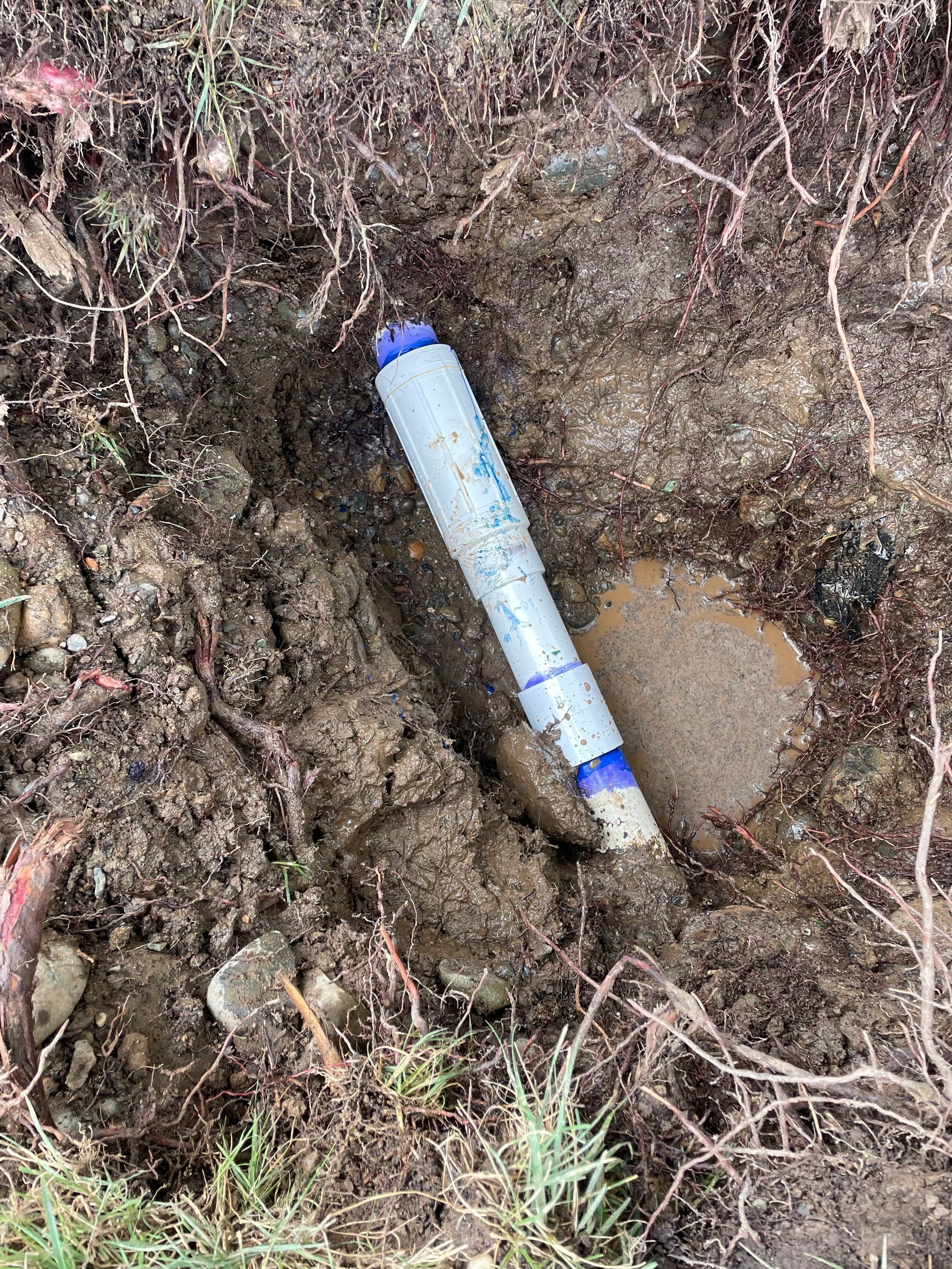 A blue pipe is laying in the dirt next to a rock.