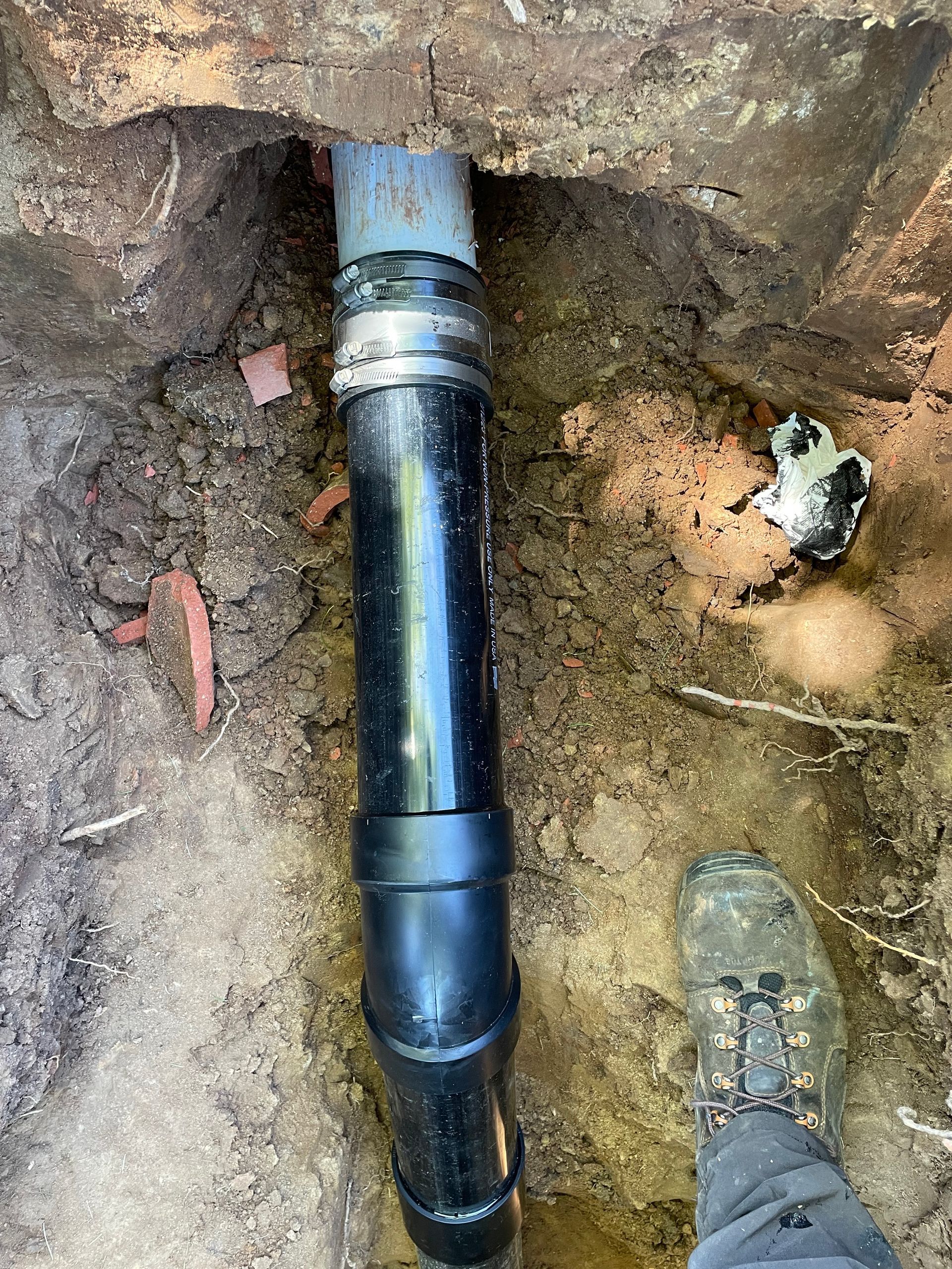A person is standing next to a black pipe in the dirt.