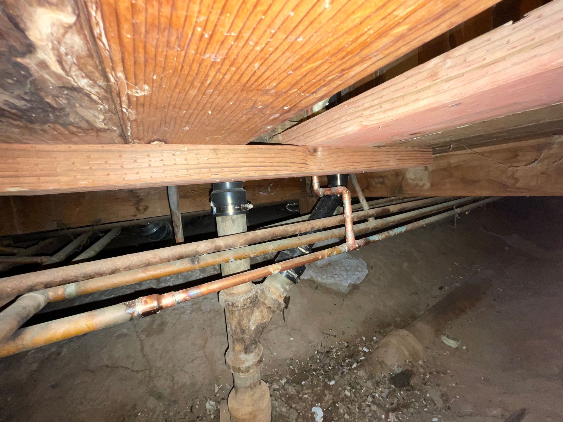 A bunch of pipes are under a wooden ceiling in a basement.