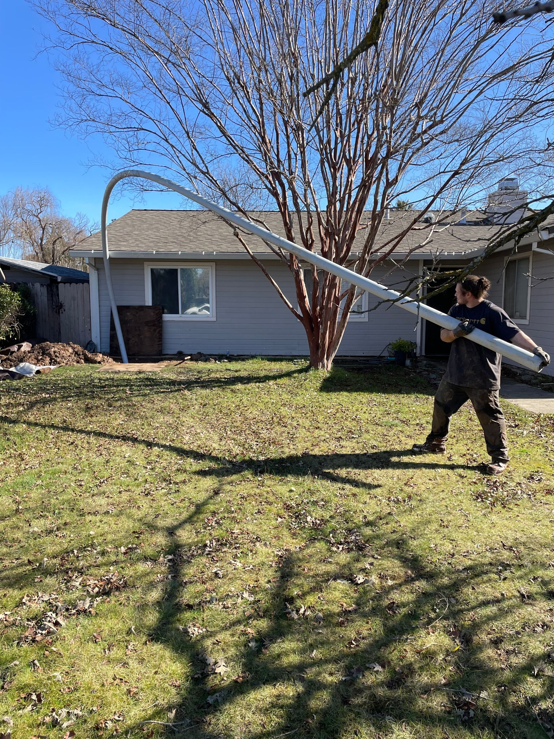 A man is holding a large pipe in a yard in front of a house.