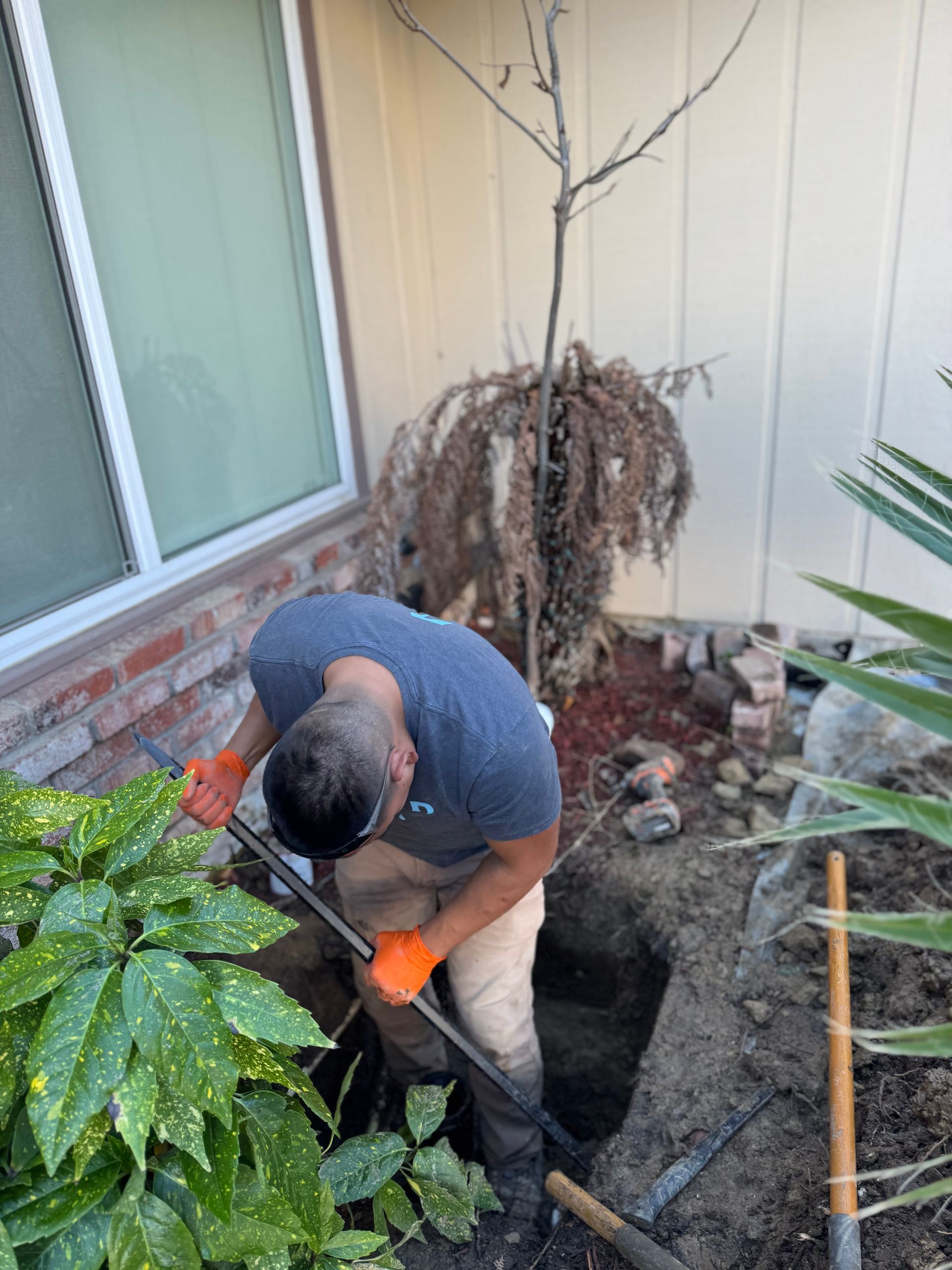 A man is digging a hole in the ground in front of a house.