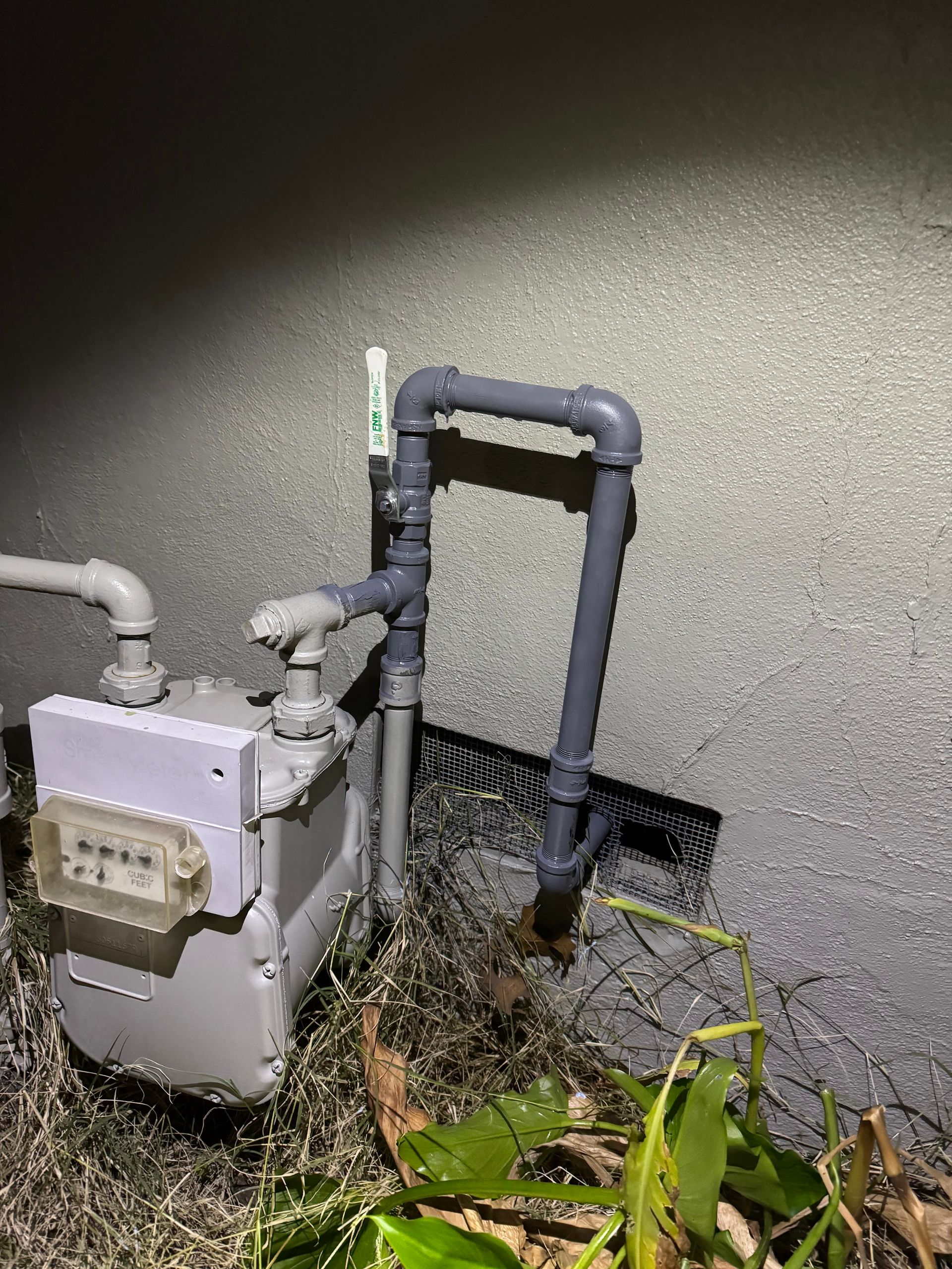 A gas meter is sitting next to a pipe on the side of a building.