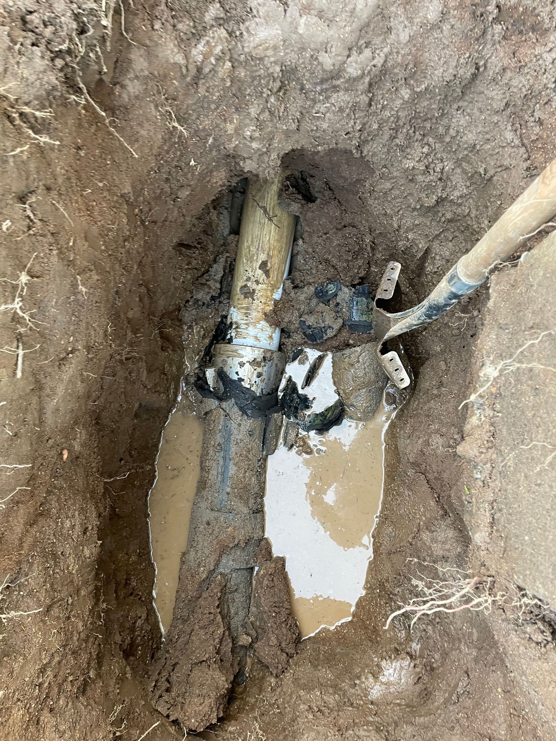 A muddy hole with a pipe in it and a shovel in it.