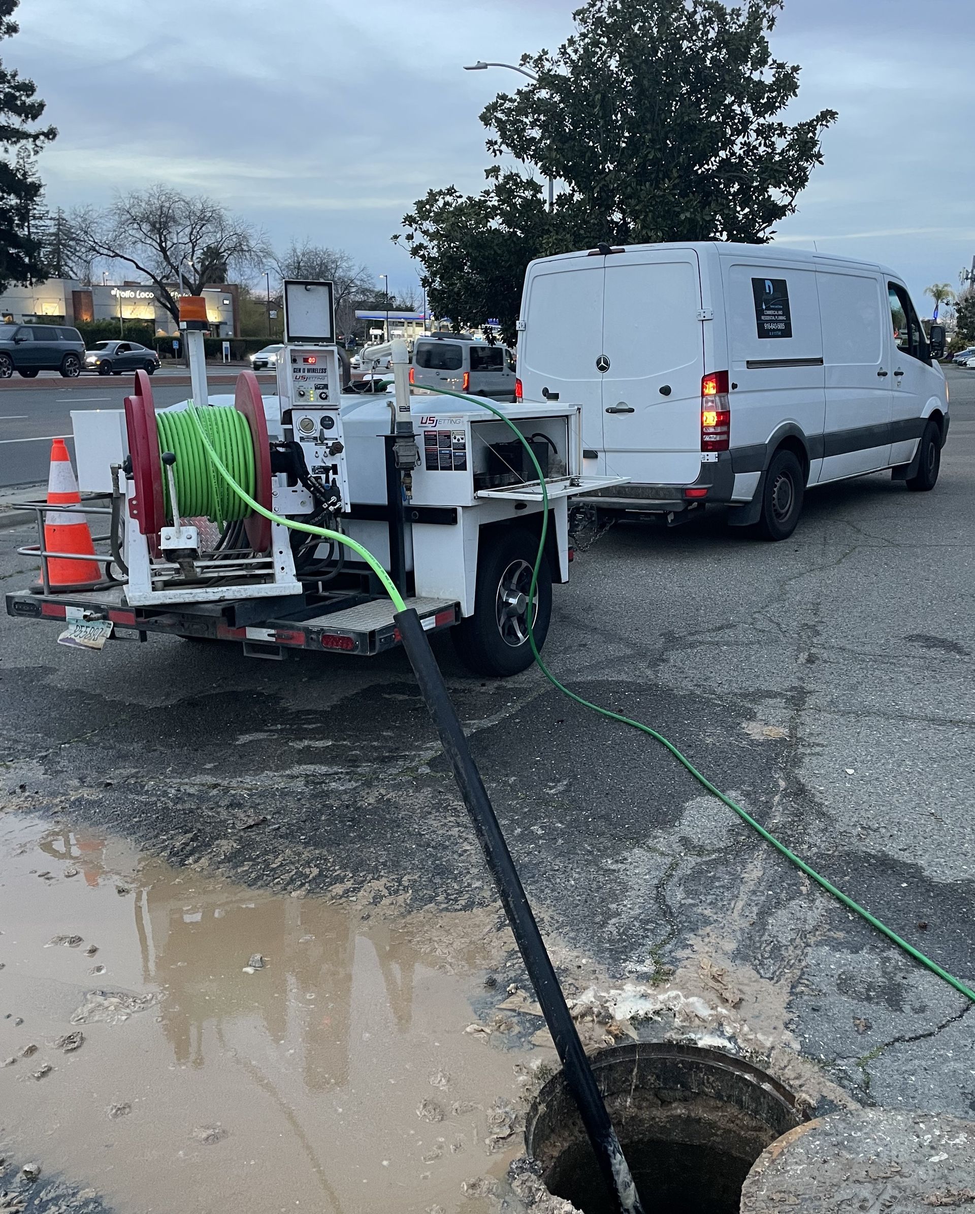A white van with a hose attached to the back is cleaning a drain.