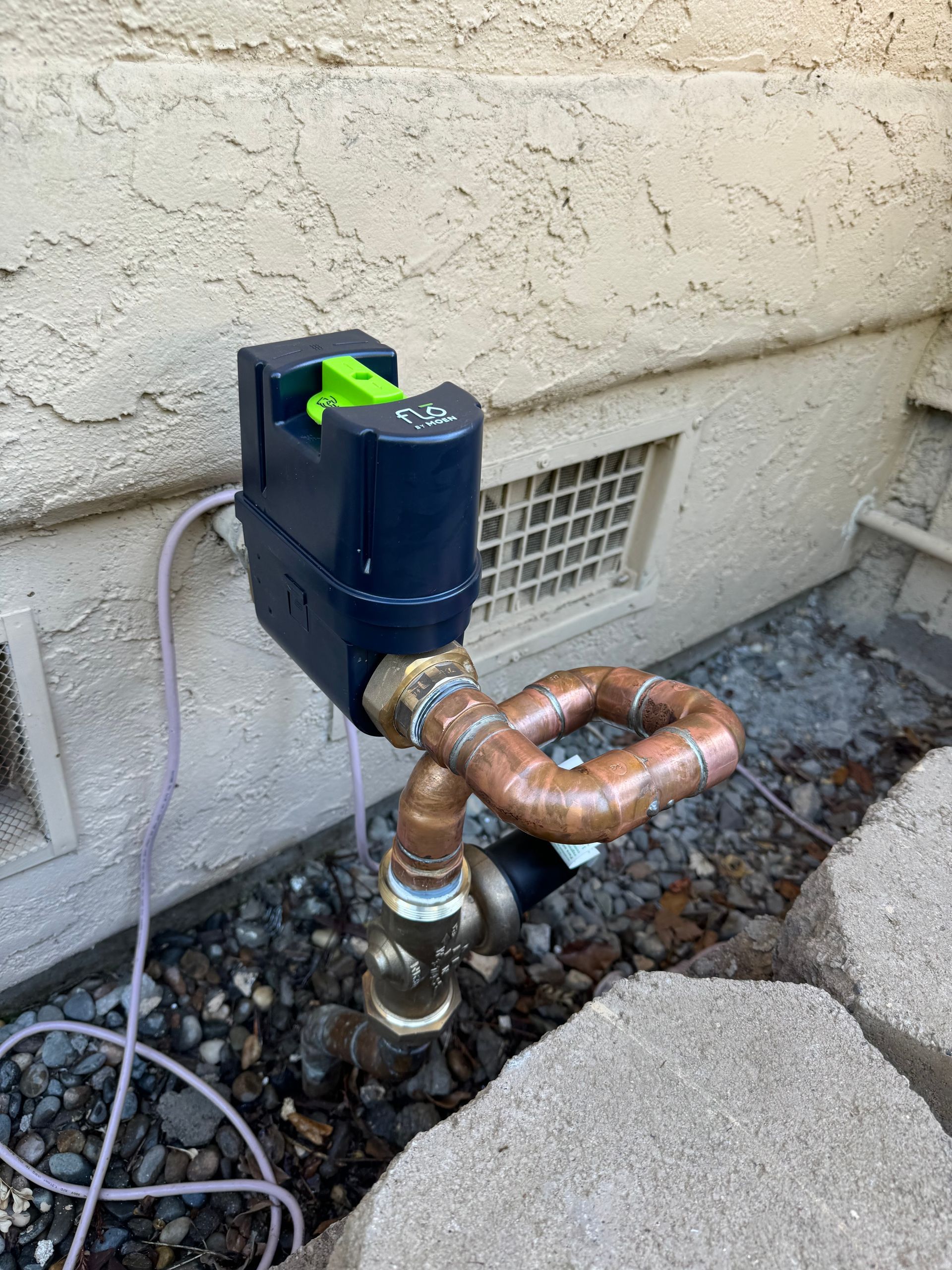 A water meter is attached to a copper pipe next to a wall.