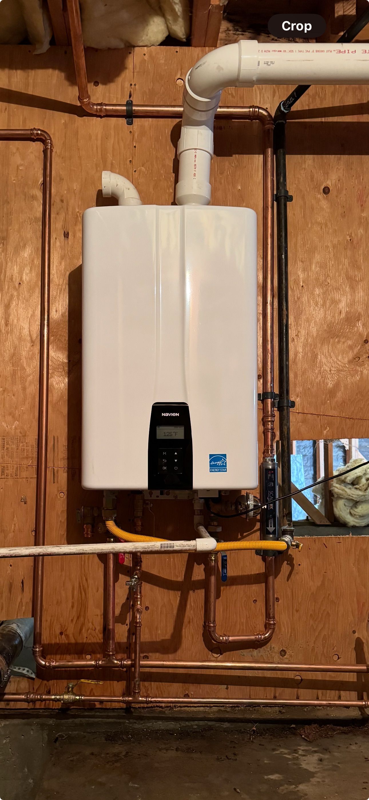 A white water heater is hanging on a wall next to copper pipes.