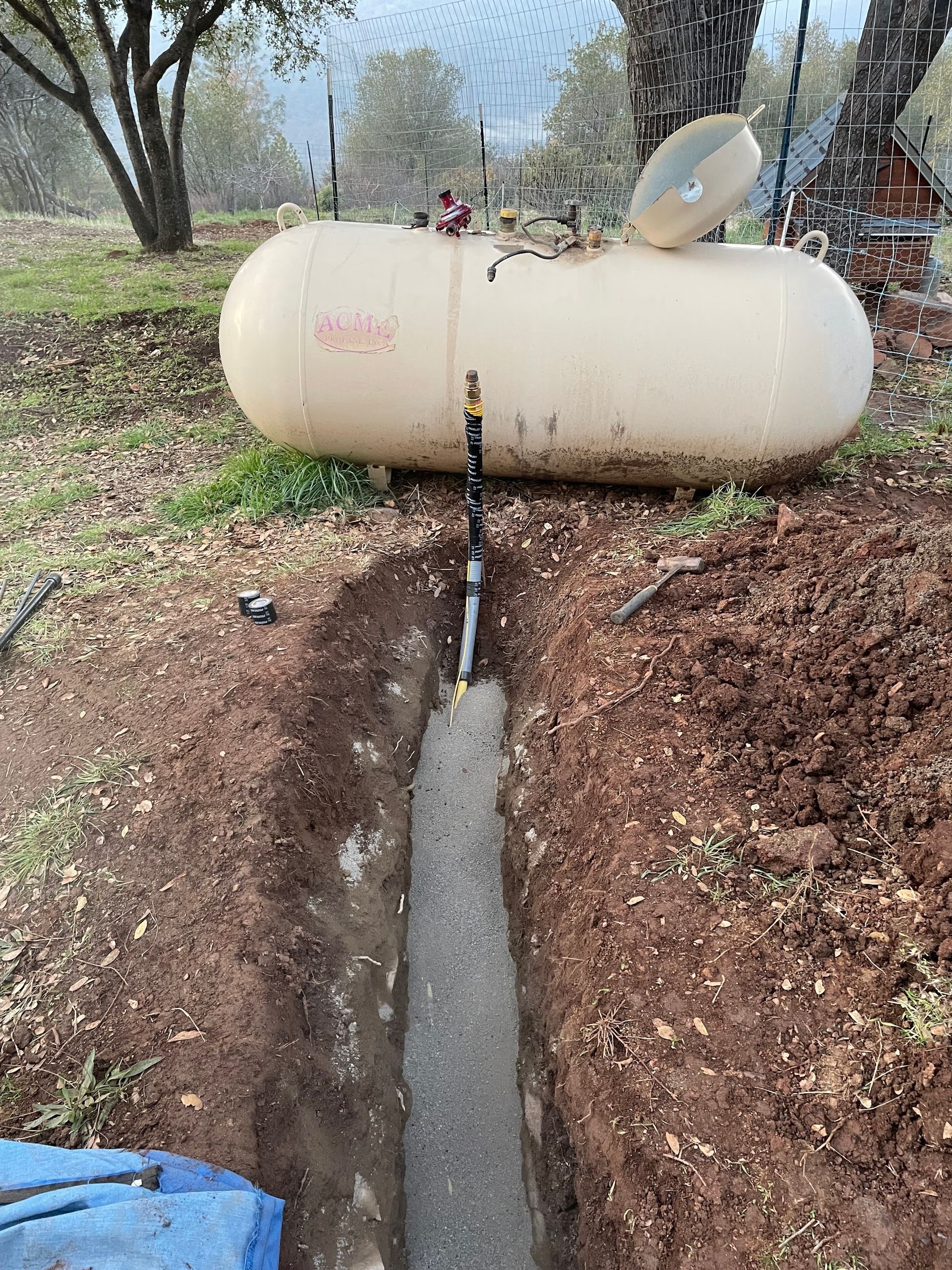 A propane tank is sitting in the dirt next to a pipe.