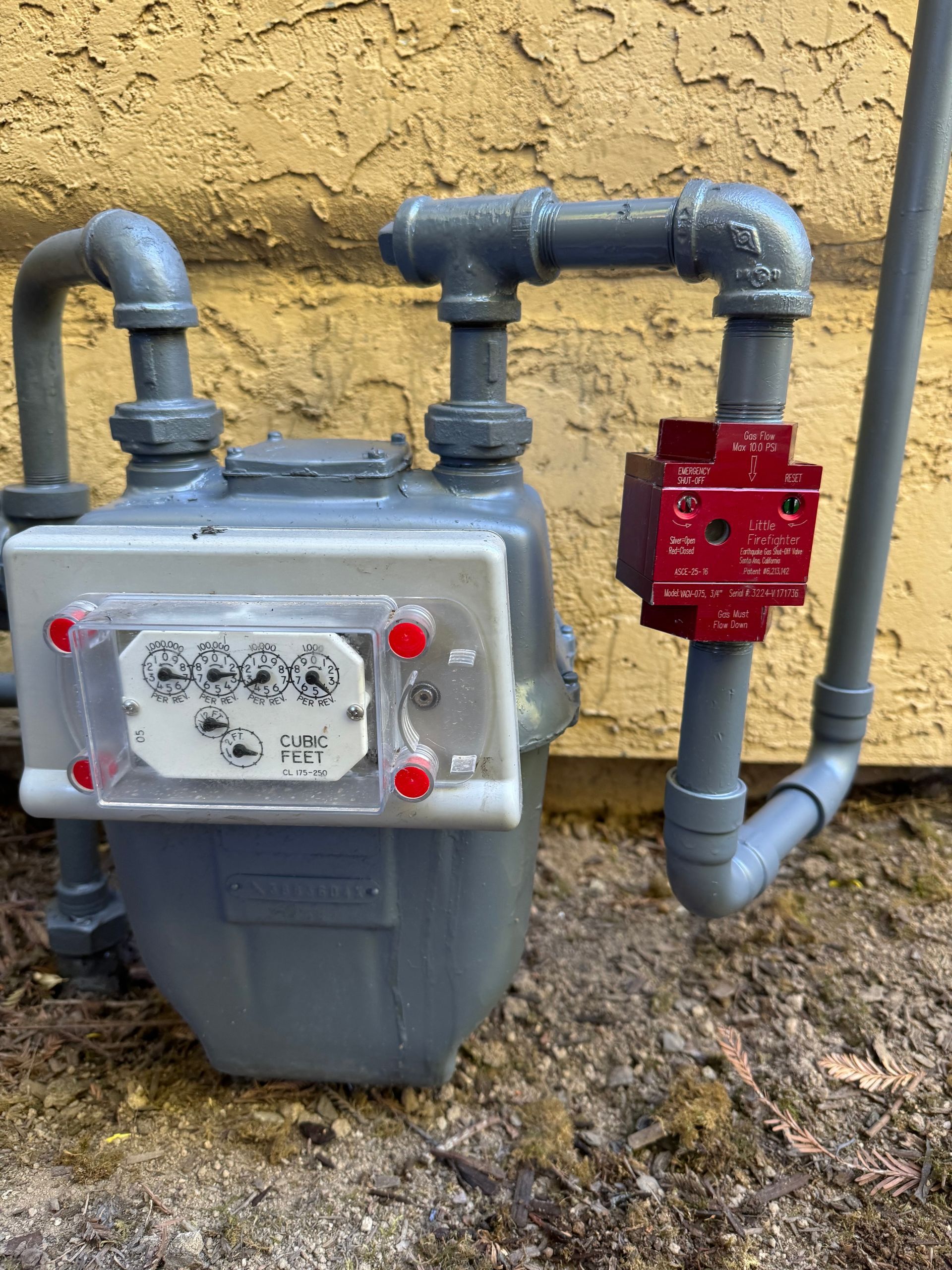 A gas meter is attached to a pipe outside of a building.