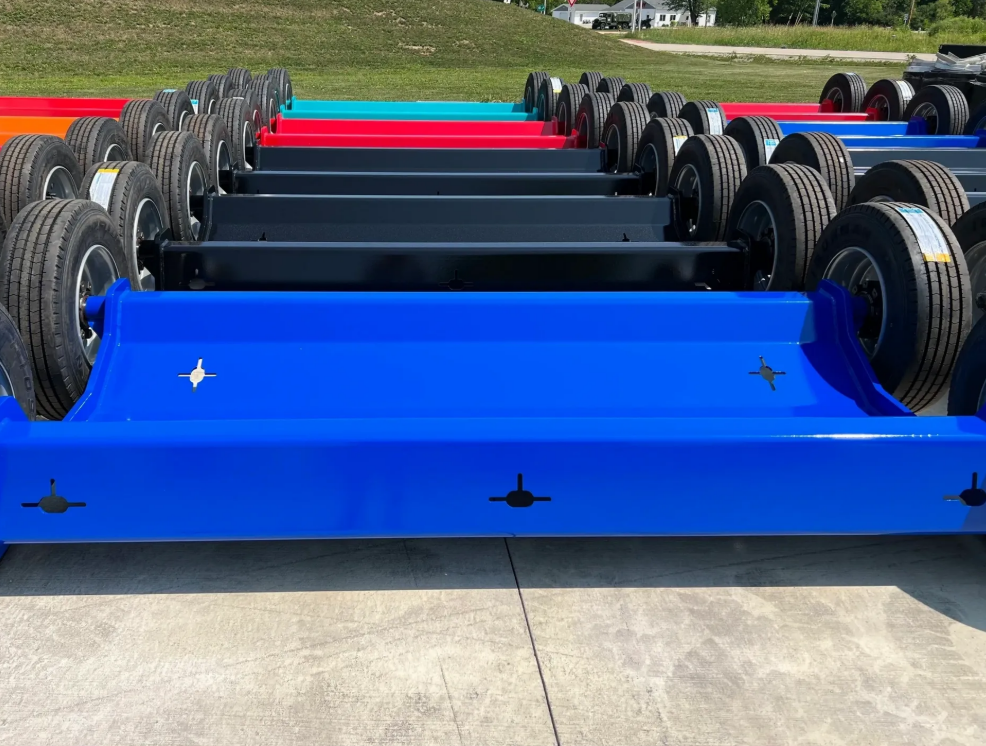 Rows of colorful trailer frames: blue, black, red, and orange, parked on concrete.
