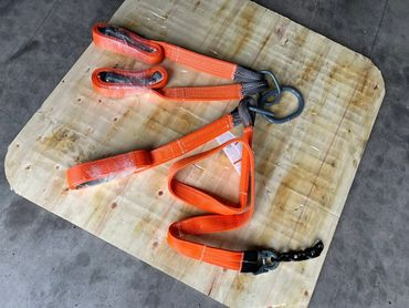 Orange rigging straps with metal hardware on a wooden surface.