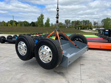 A large gray metal structure with wheels is suspended by straps and a crane hook outside.