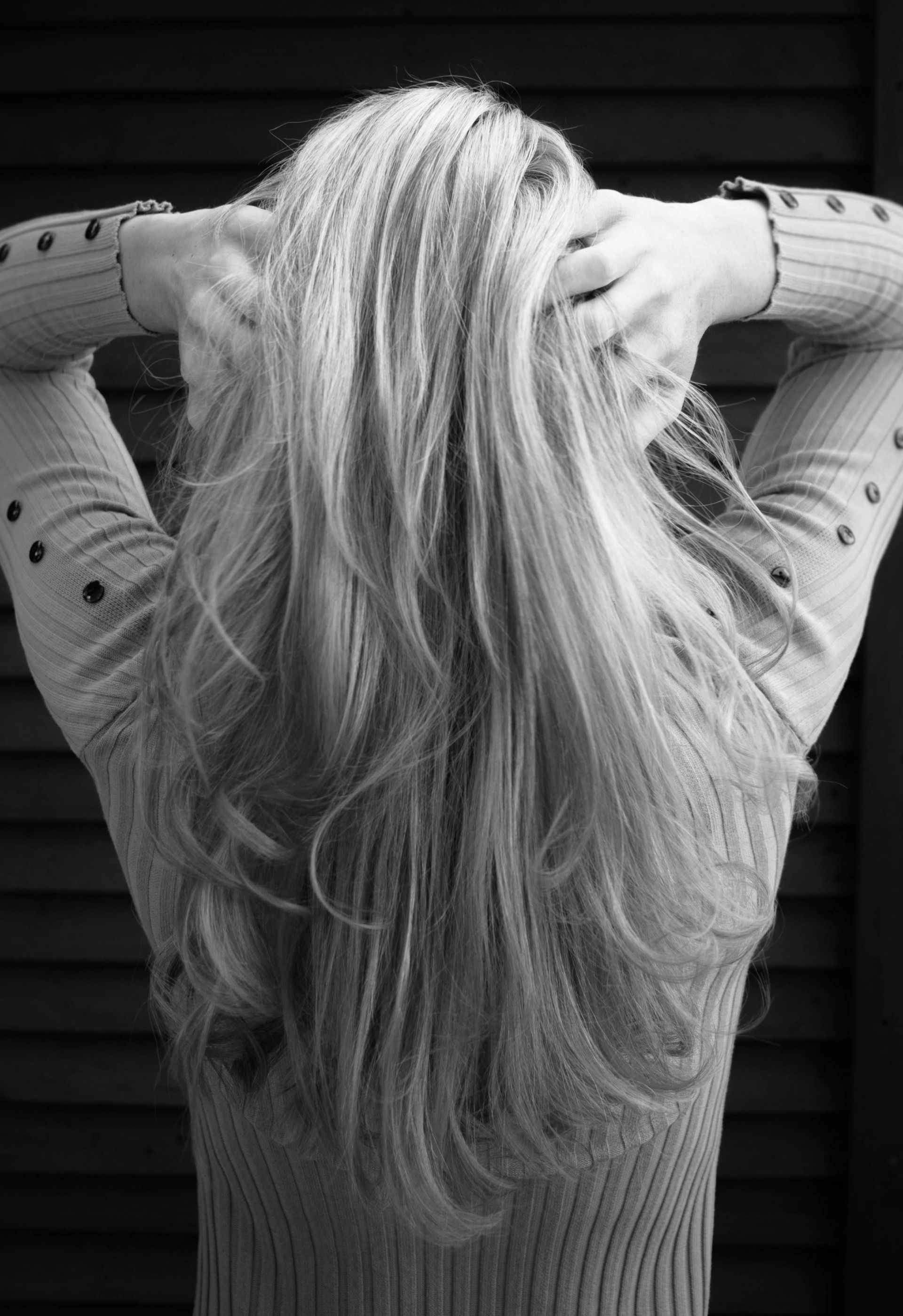 A woman with long blonde hair is holding her hair in a black and white photo