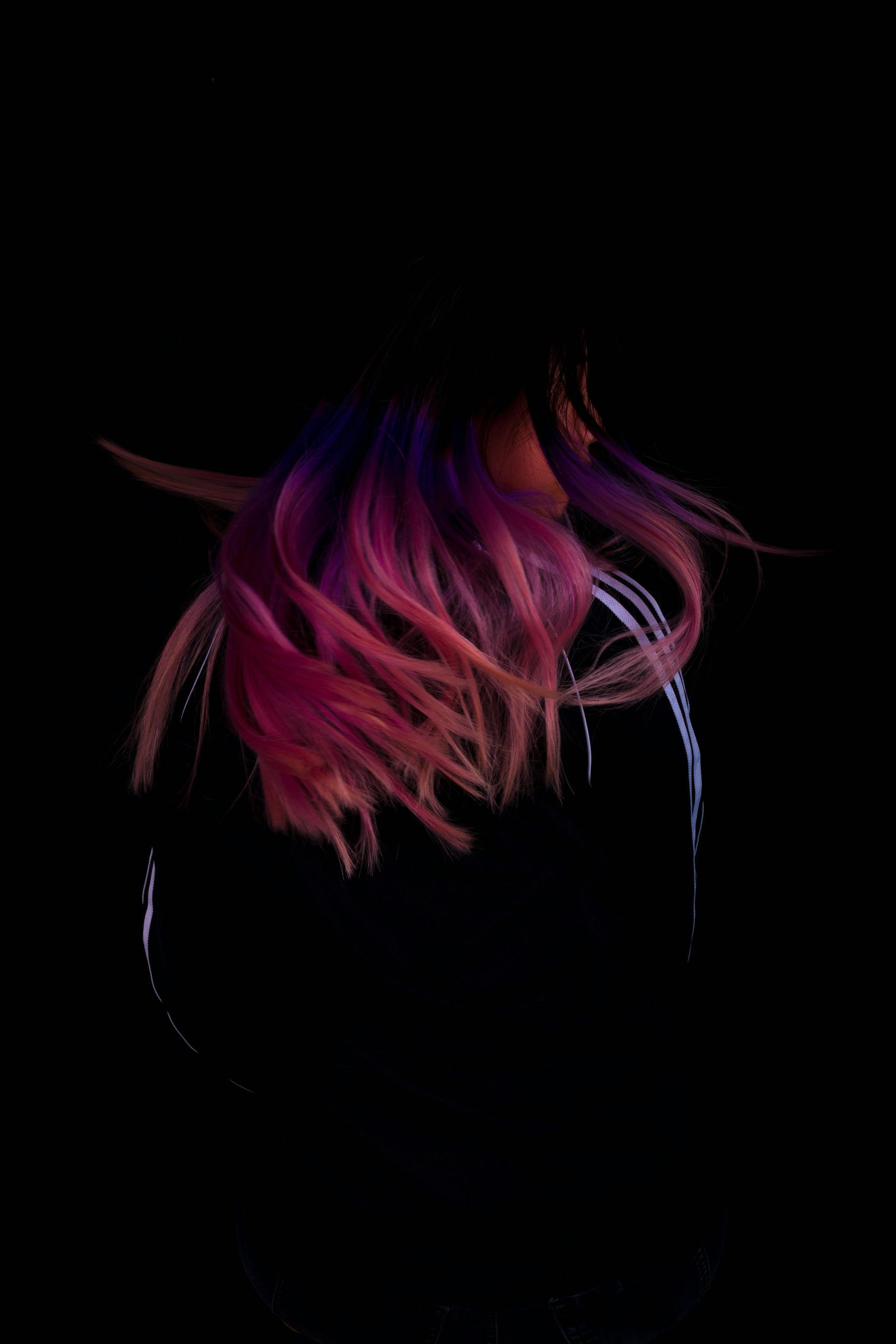 A woman with pink and purple hair is dancing in the dark