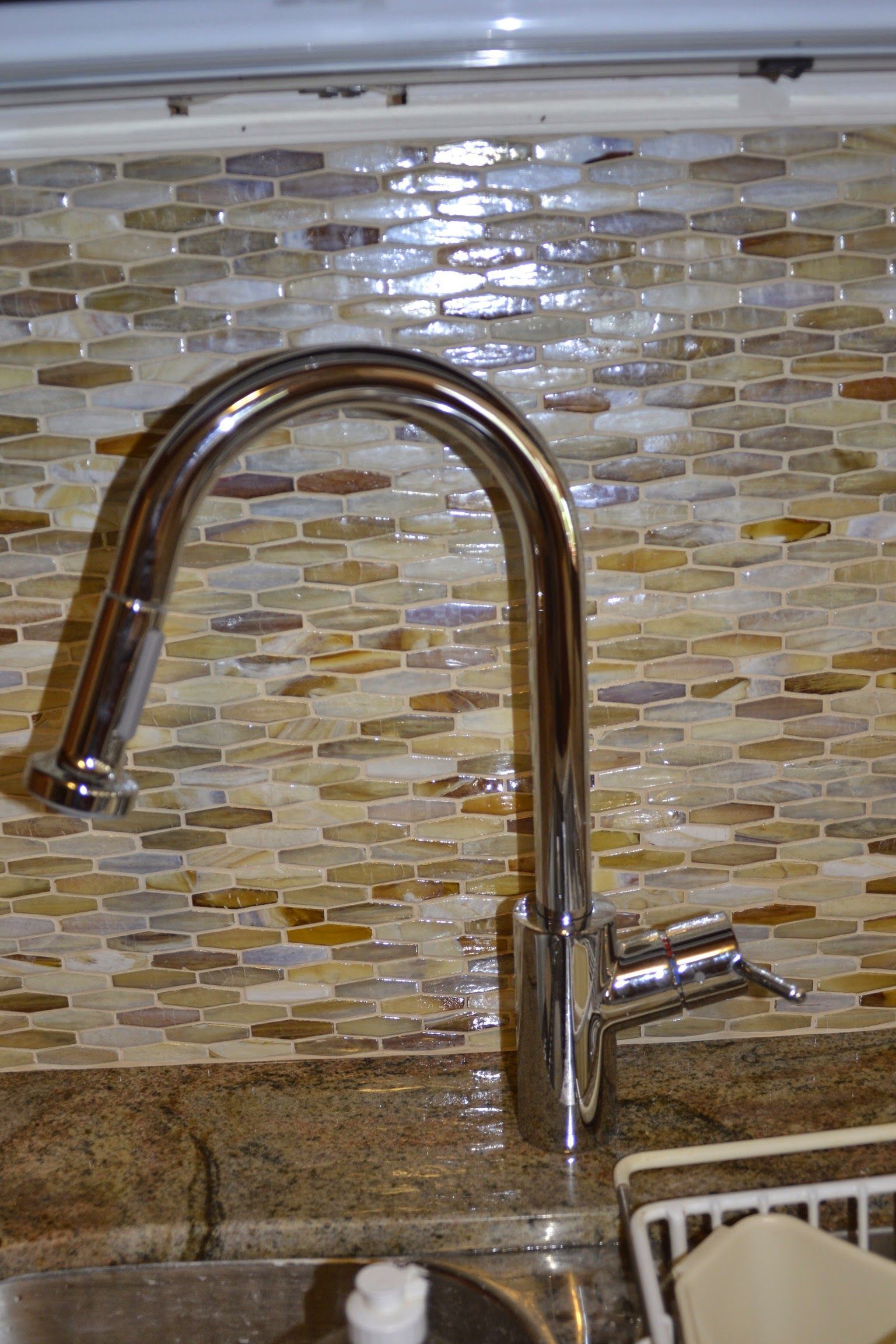 A close up of a kitchen sink faucet with a tiled wall in the background.