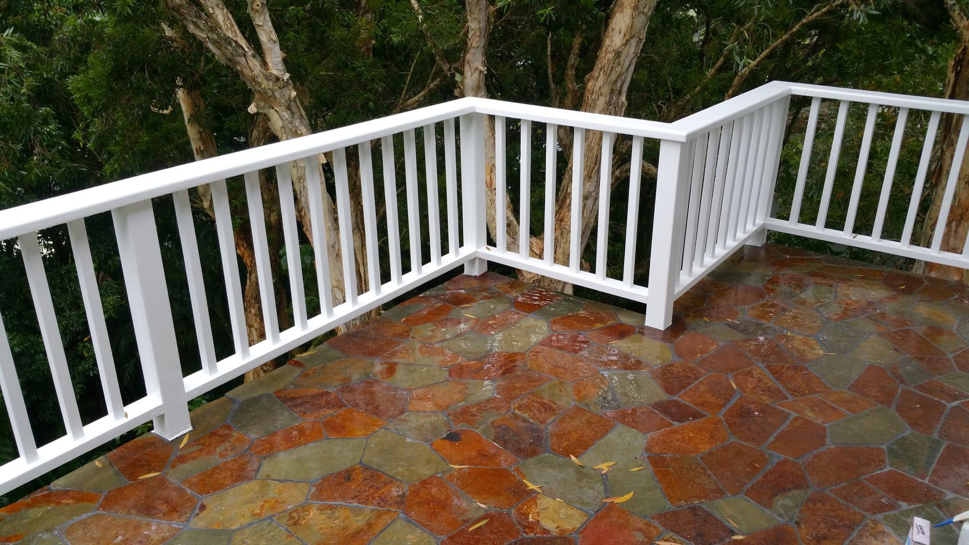 A white railing on a deck with trees in the background.