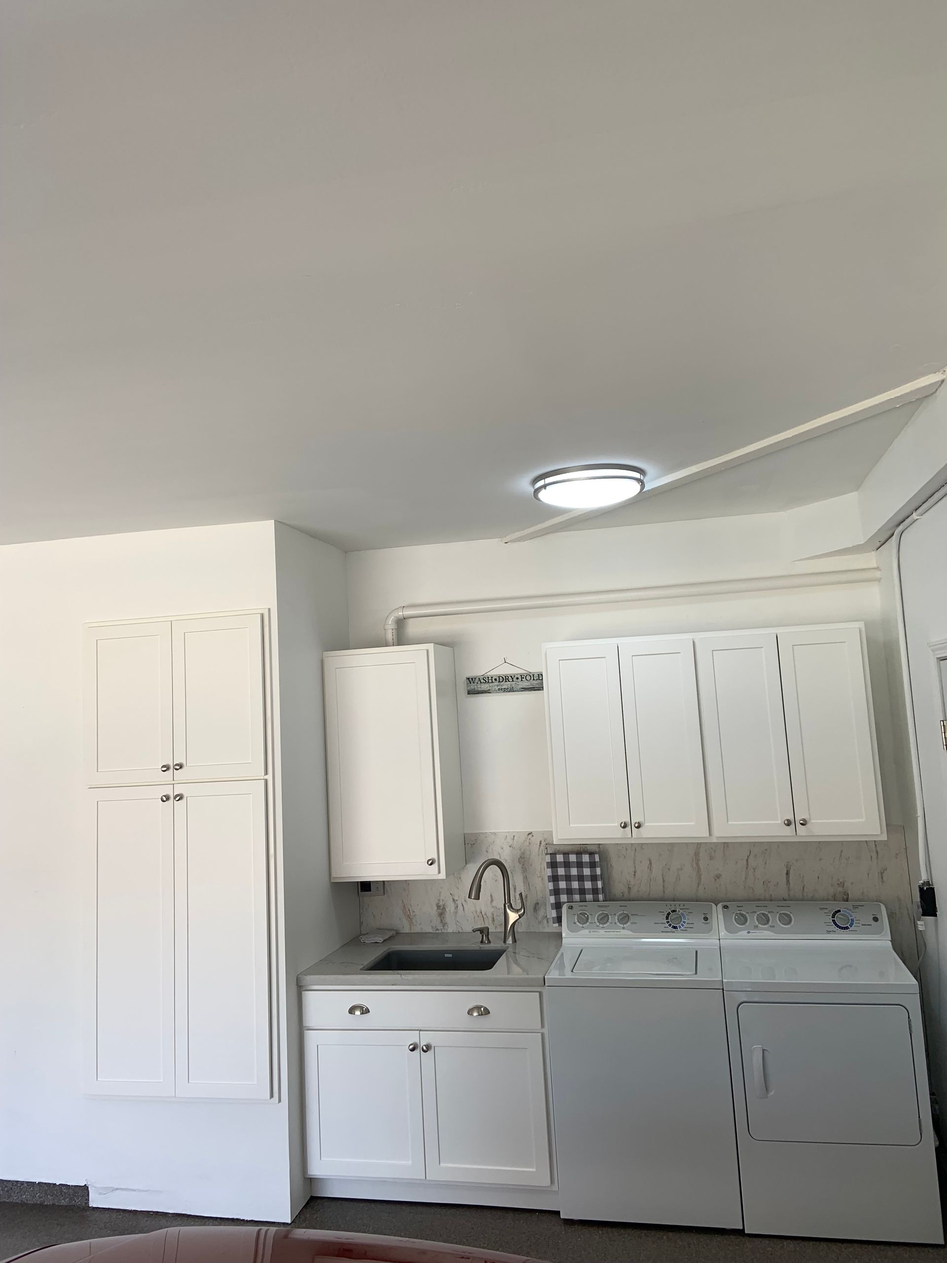 A kitchen with white cabinets , a washer and dryer , and a sink.