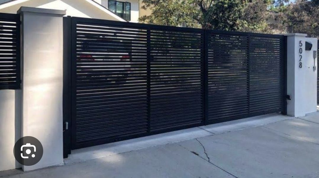 A Black Metal Gate is Surrounding a Brick Wall and a Driveway — Fence Factory In Berrimah, NT