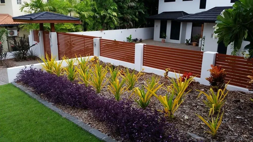 A large brown fence with white concrete pillars and a garden out the front — Fence Factory In Palmerston, NT