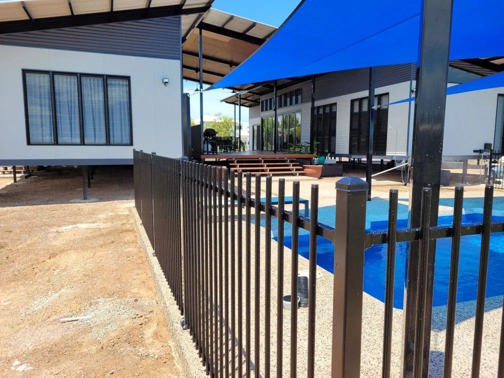 A Fence Surrounds a Swimming Pool in Front of a House — Fence Factory in Berrimah, NT