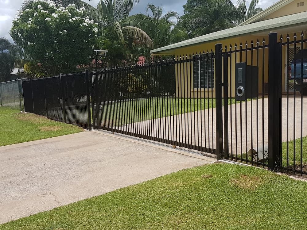A Black Fence Surrounds A Driveway in Front of A House — Fence Factory In Berrimah, NT