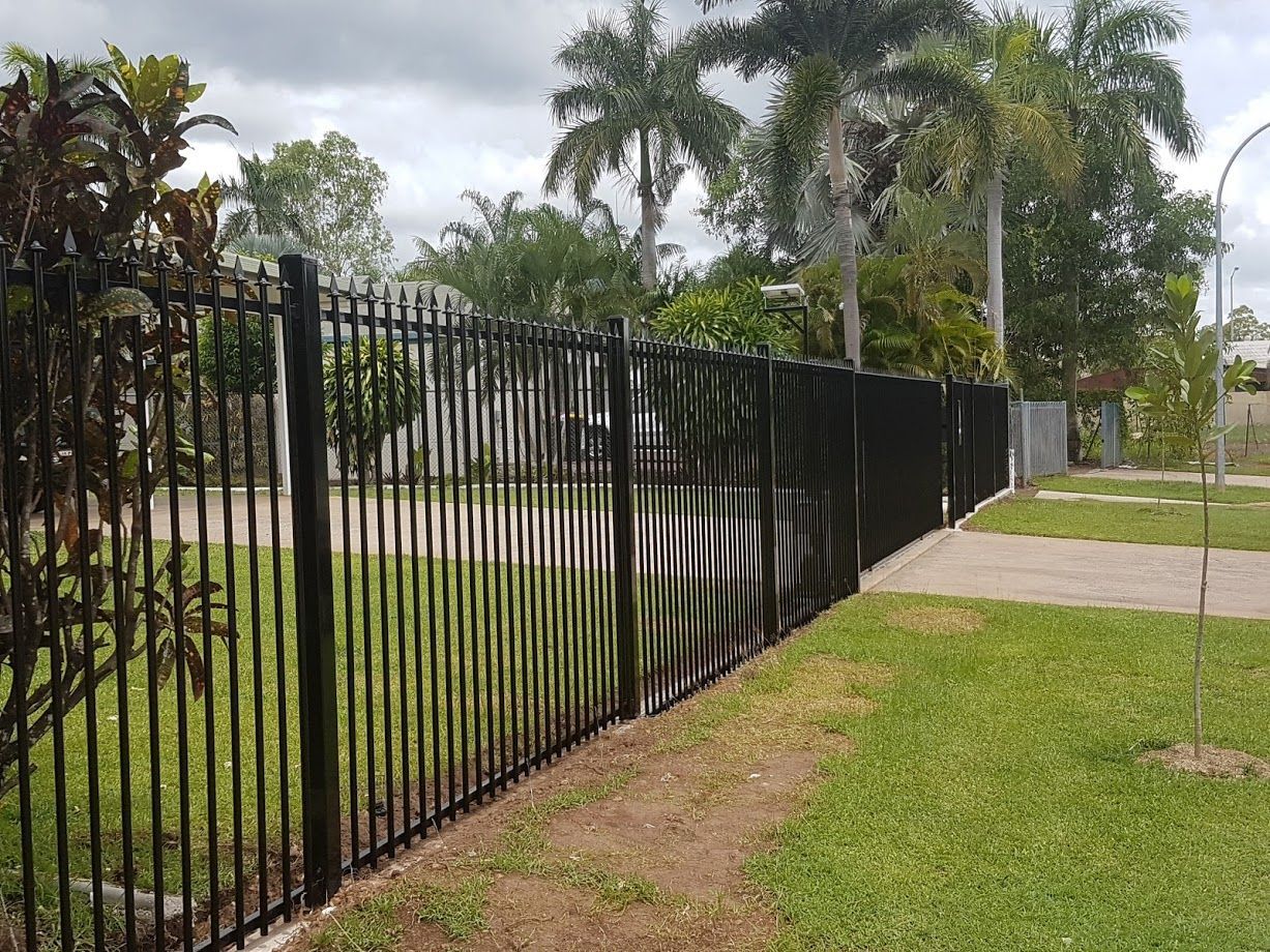 A Black Fence Is Surrounded by Grass in Front of A House — Fence Factory In Palmerston, NT