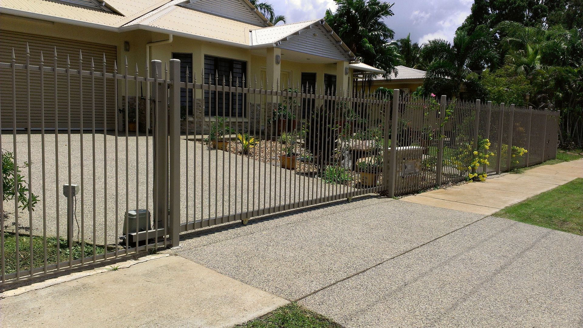 A Brown Metal Fence is Surrounding a Brick Wall and a Driveway — Fence Factory In Berrimah, NT