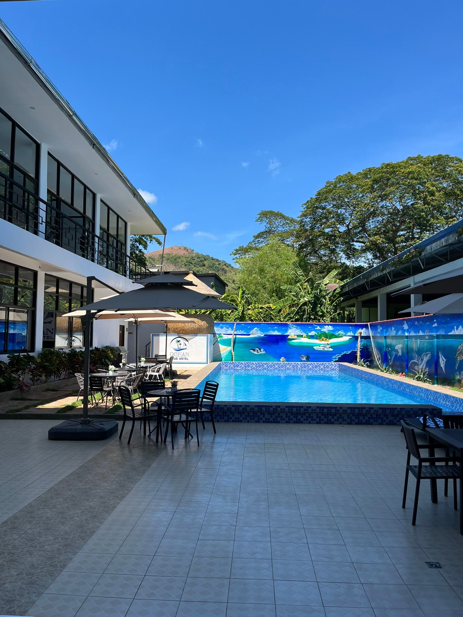 A large swimming pool surrounded by tables and chairs in front of a building.
