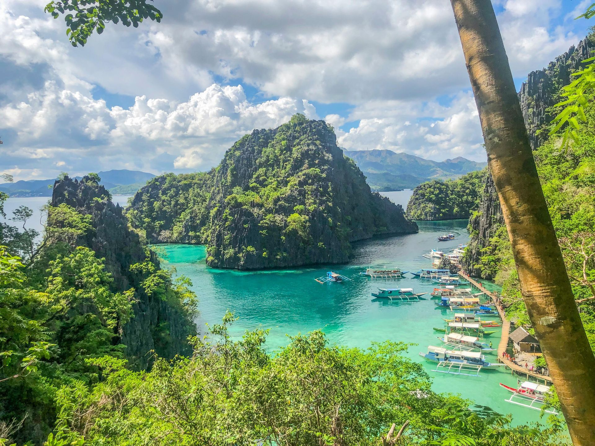 A view of a tropical island with boats in the water and mountains in the background.