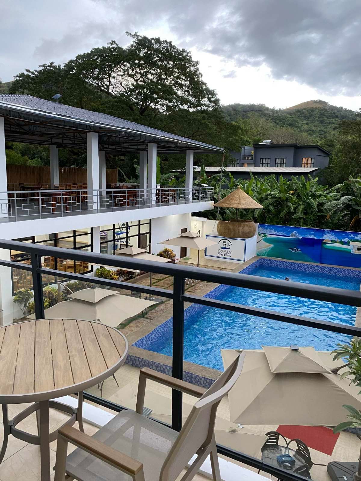 A balcony with a table and chairs overlooking a swimming pool.