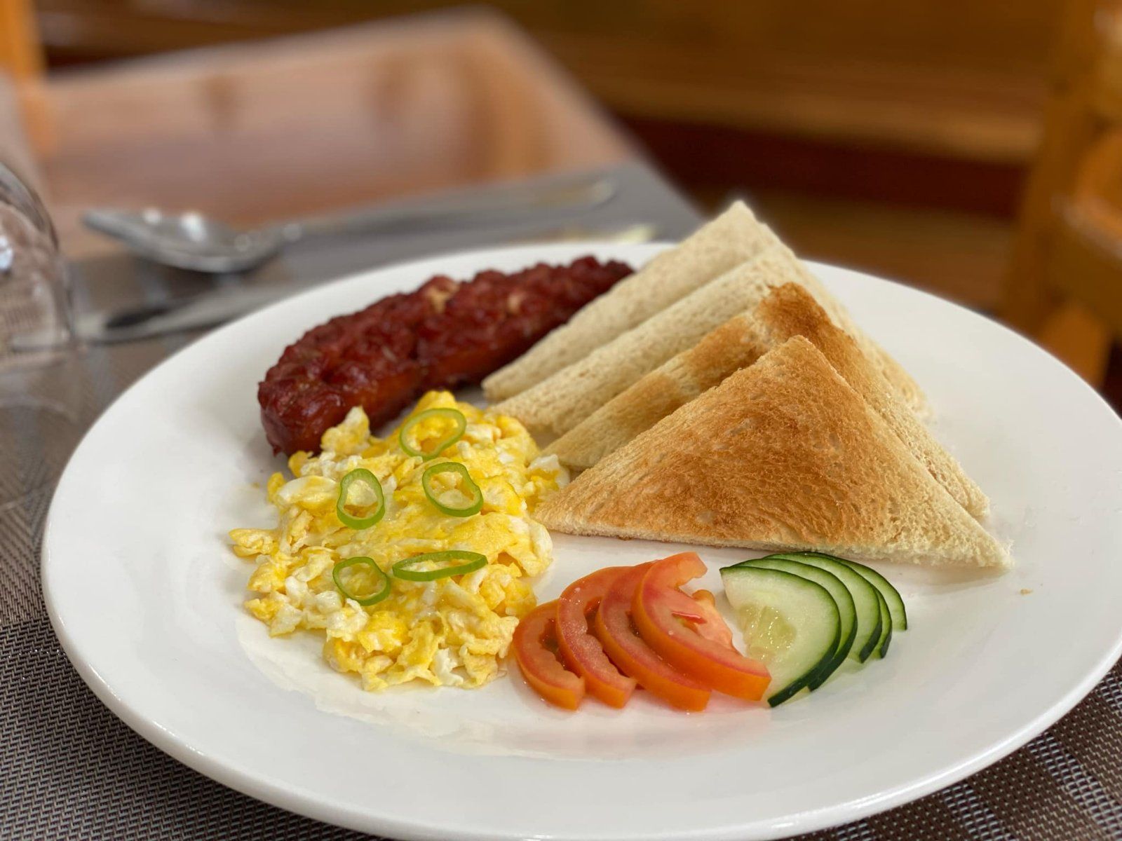 A white plate topped with scrambled eggs , sausage , tomatoes , cucumbers and toast.
