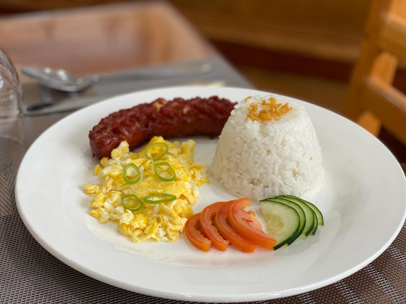 A white plate topped with rice , scrambled eggs , tomatoes and cucumbers.