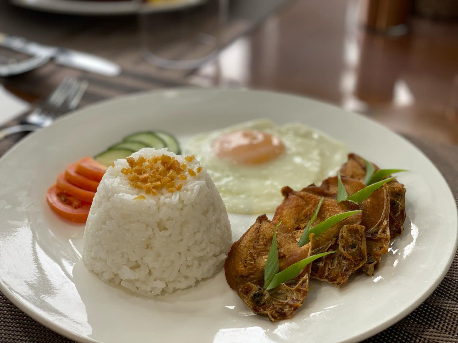 A plate of food with rice , fried chicken , eggs and vegetables on a table.