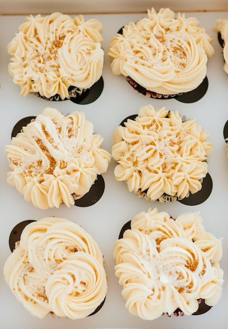 A box of cupcakes with frosting on them are sitting on a table.