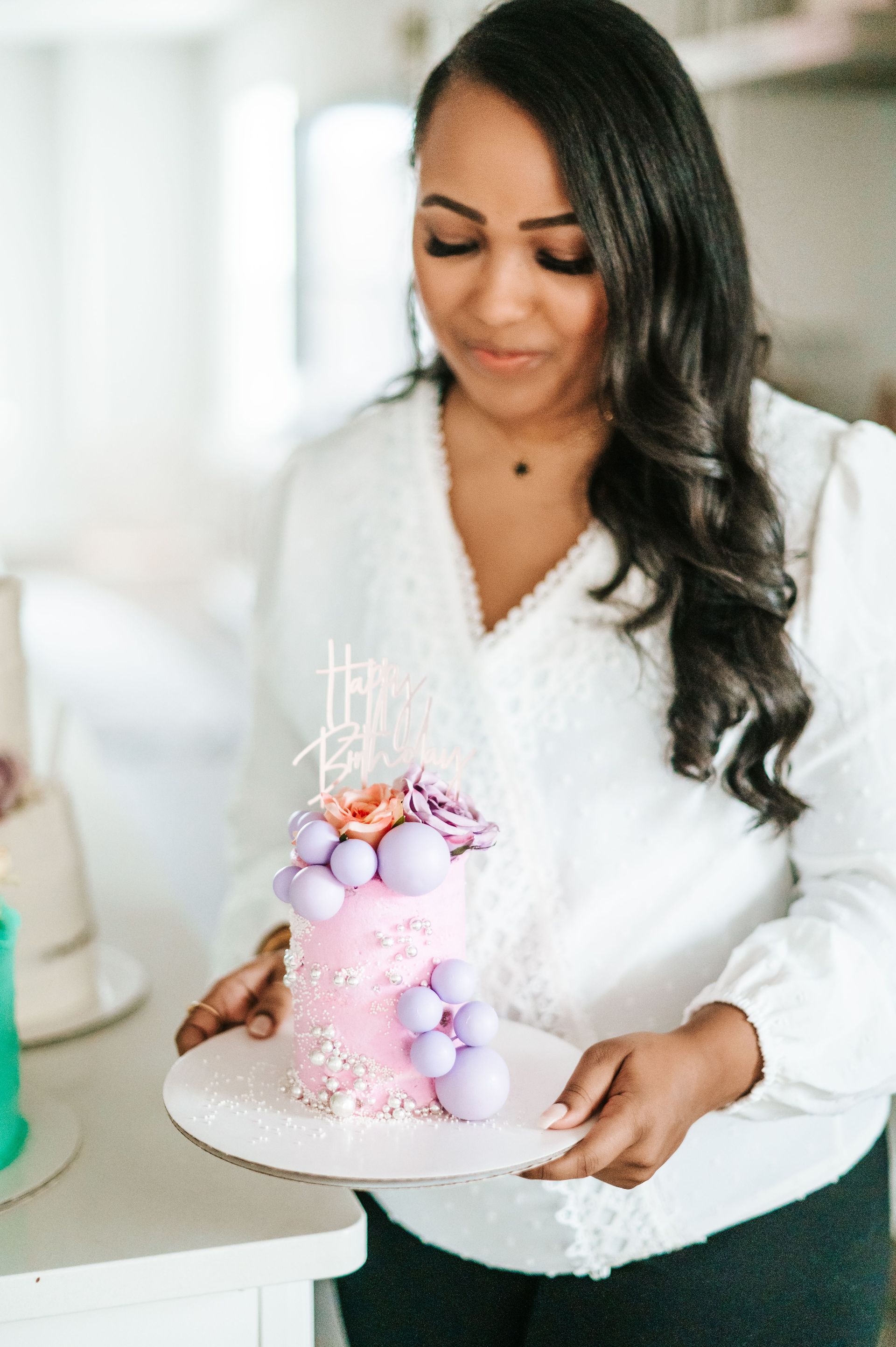 A woman is holding a pink and purple cake on a tray.