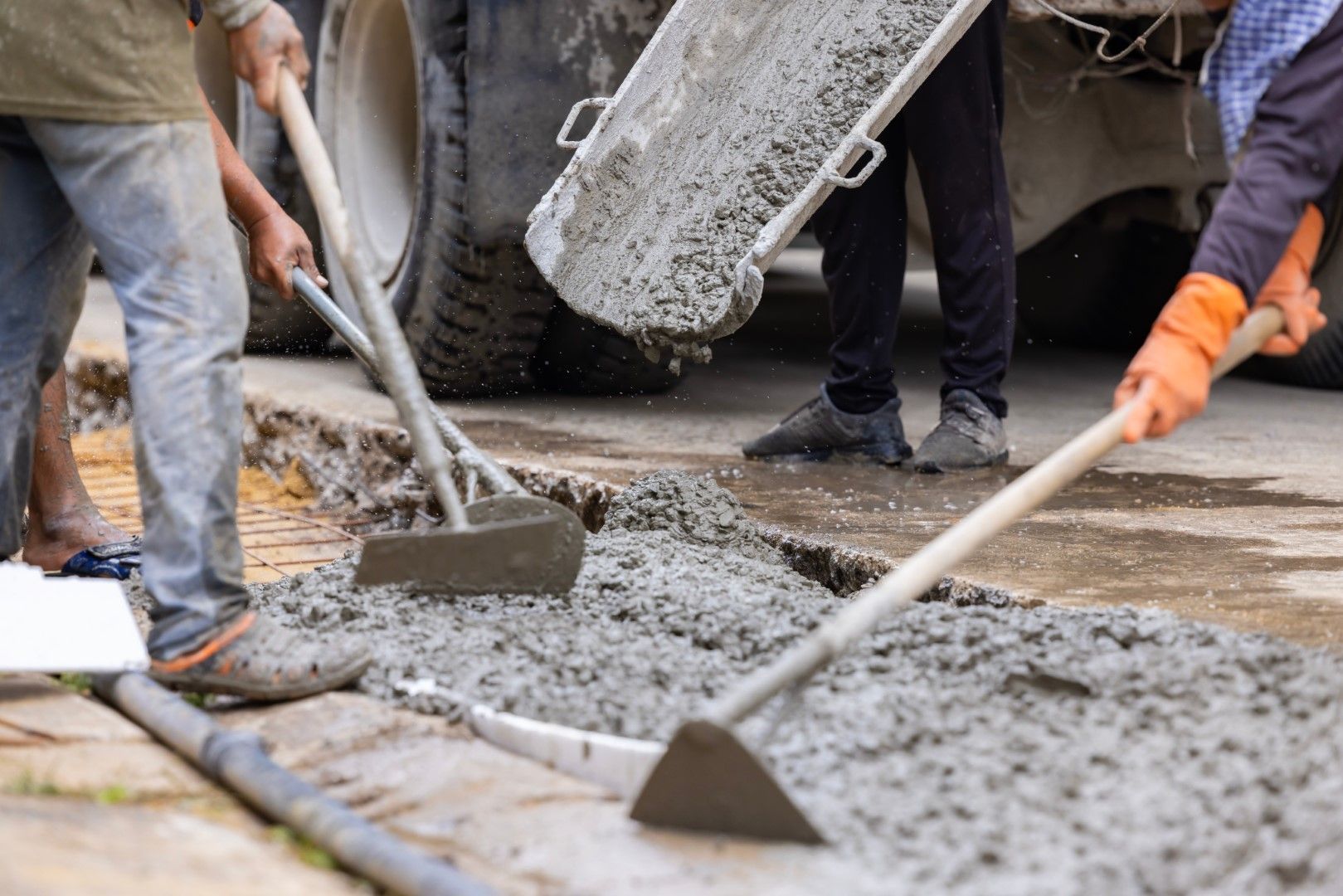 Workers using shovels to spread wet concrete from a truck on a construction site.